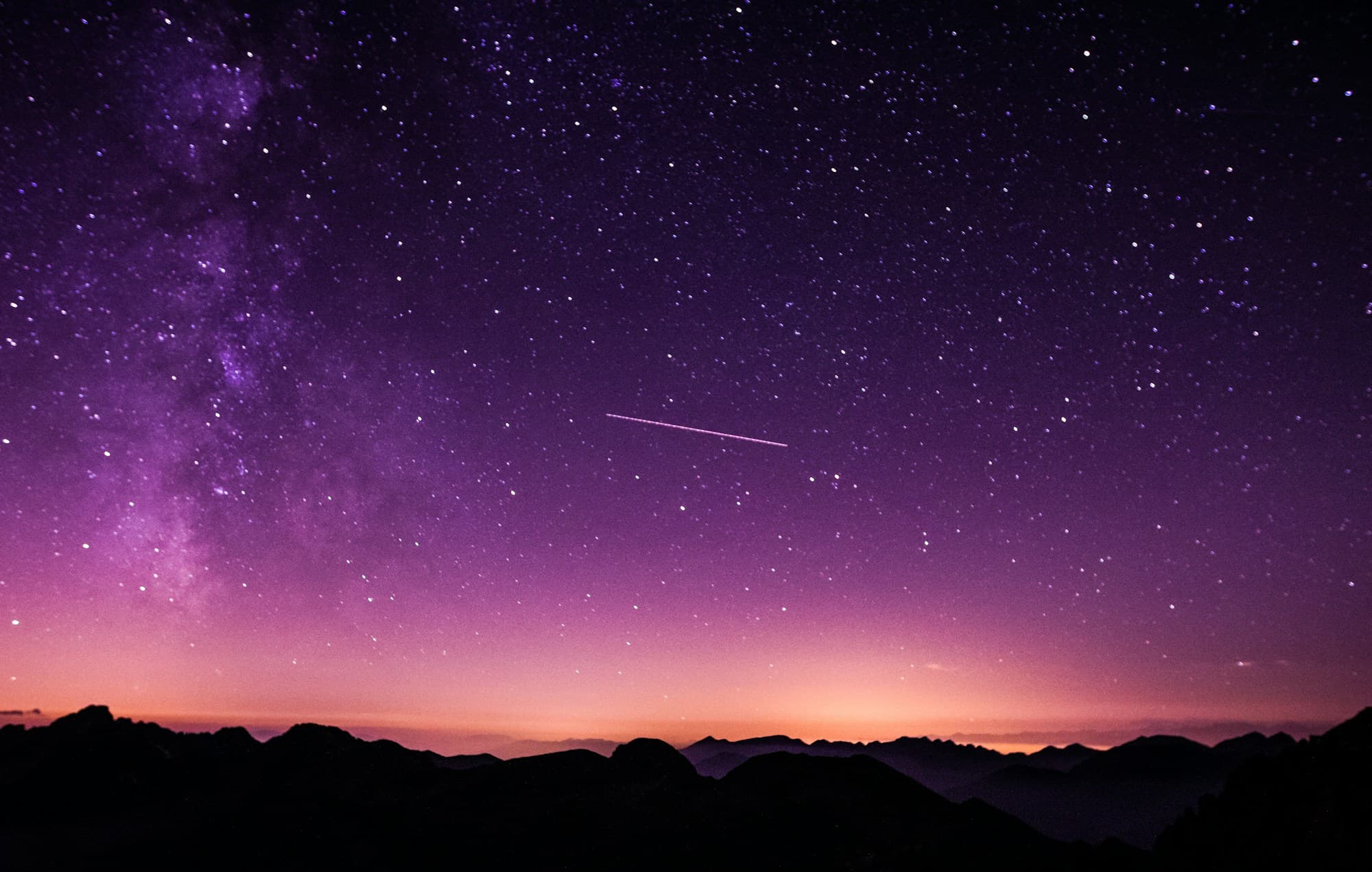 Night sky with stars and the Milky Way over a dark landscape.